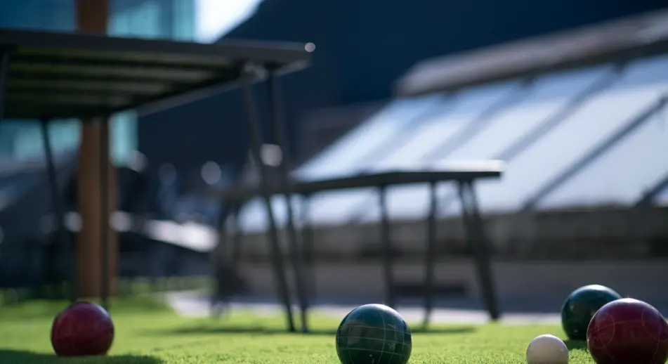 Picture of the Next/Now rooftop, bocce balls on grass in foreground, tables in background